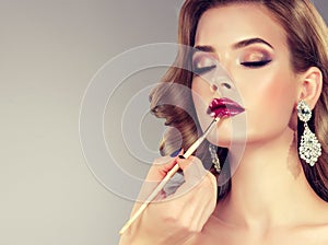 Hand of make-up master is painting lips of young beautiful brunette model.