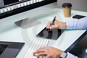Hand of male designer working at his desk using stylus and digital graphics tablet