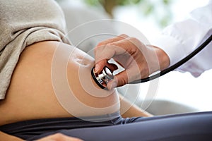 Hand of male obstetrician doctor with stethoscope listening to pregnant woman baby heartbeat.