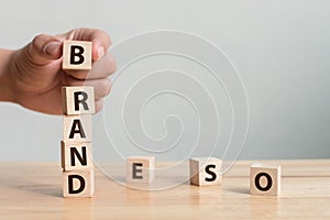 Hand of male putting wood cube block with word â€œBRANDâ€ on wooden table. Brand building for success concept