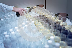 The hand of a male waiter pours wine into glasses at a cocktail reception, red wine in a glass white drink in a wine