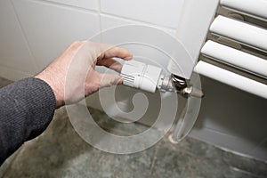 Hand man adjusting home thermostat on white heating radiator