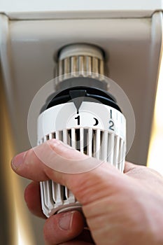 Hand of man adjusting radiator thermostat valve to number 1 icon, symbol for saving money at heating costs or low temperature