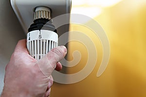 Hand of man adjusting radiator thermostat valve to number 5 icon, symbol for high heating costs or warm temperature setting