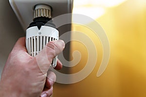 Hand of man adjusting radiator thermostat valve to snow flake frost icon, symbol for saving money at heating costs or low