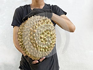 The hand of a man in black raises a large durian fruit