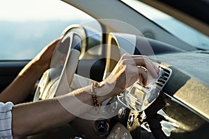 Hand of man with bracelets wipes panel vent with white napkin holding steering wheel driving car