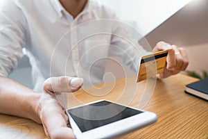 Hand of man in casual shirt paying with credit card and using smart phone for online shopping making orders via the Internet using