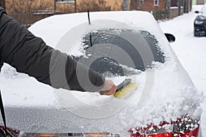 The hand of a man clearing snow from the rear window of a car with a brush