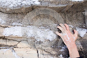 The hand of a man clings to a ledge on a stone. Rock covered with snow