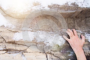 The hand of a man clings to a ledge on a stone. Rock covered with snow