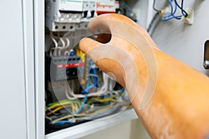 The hand of a man in a dielectric glove with a screwdriver moves towards the switchboard photo