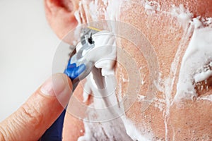 Hand man with a disposable razor shaving his cheek closeup