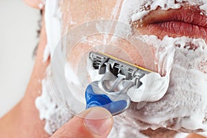 Hand man with a disposable razor shaving his face closeup