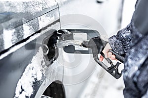 Hand of a man filling up the fuel tank of his car during freezing snowy winter