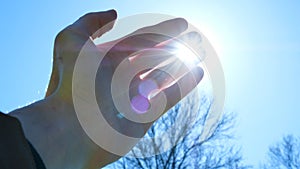 Hand of man fingers plays with the sun`s rays against the blue sky