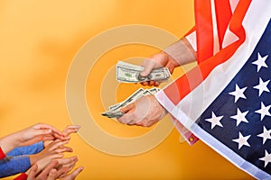 The hand of a man flying the American flag hands money to childrenï¿½s hands, the concept of dependence on the USA