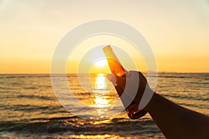 Hand of man is holding beer bottle and holds his hand up on the sky in evening with sunset. celebrating on holiday at the beach in