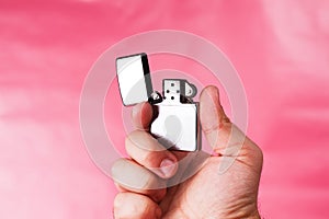 Hand of a man holding cigarette lighter against light pink.