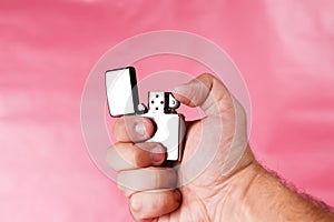 Hand of a man holding cigarette lighter against light pink.