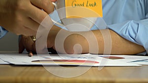 Hand man holding a coffee cup and put it down on the Annual report on coffee cup have a sticky note that says good luck. The conce