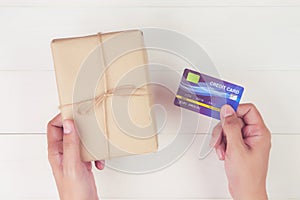 Hand of man holding credit card and online shopping for giving gift box with kraft paper on wooden background.