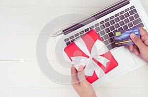 Hand of man holding credit card and online shopping for giving gift box with laptop computer on wooden background.