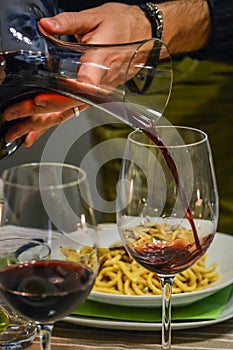 Hand of a man holding a decanter and pouring red wine in a glass