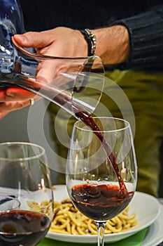 Hand of a man holding a decanter and pouring red wine in a glass