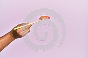 Hand of man holding fish nigiri with chopsticks over isolated pink background