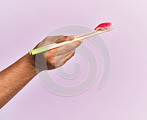 Hand of man holding fish nigiri with chopsticks over isolated pink background