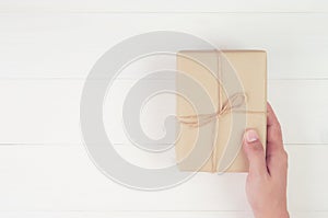 Hand of man holding gift giving on wooden table in Christmas day or holiday, present box for anniversary or birthday.