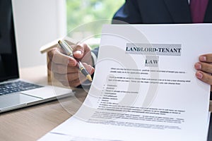 The hand of a man holding a house purchase contract with a pen showing up to customers. House salesman is showing Landlord-Tenant