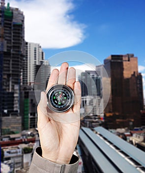 The hand of a man holding a magnetic compass over a city buildings