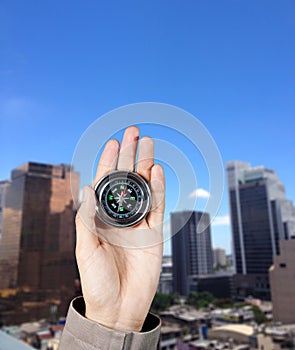 The hand of a man holding a magnetic compass over a city buildings