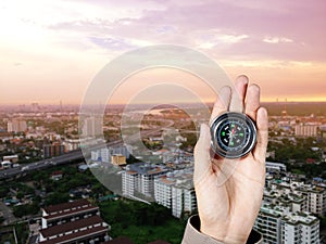 The hand of a man holding a magnetic compass over a city buildings