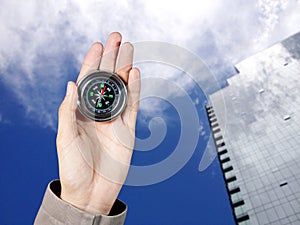 The hand of a man holding a magnetic compass over a city buildings