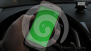 Hand of man holding mobile smart phone with chroma key green screen in car