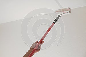 Hand of a man holding a paint roller on a long telescopic pole to paint the ceiling while renovating an apartment, housing concept