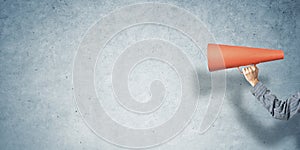 Hand of man holding paper trumpet against concrete background