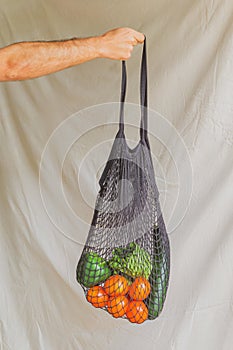 Hand of a man holding a reusable cotton bag with eco vegetables inside. Eco friendly lifestyle. Real fooding photo