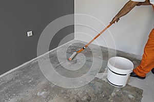 The hand of a man holding a roller and puts primer on cement flo