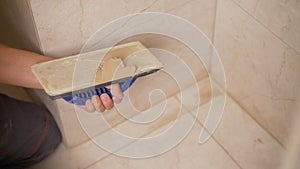 The hand of man holding a rubber float and filling joints with grout. The worker is rubbing the tiles with a float photo