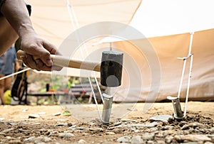 Hand of man holding a rubber mallet,hammering aluminium steel tent stakes pegs nail,fastening tent for camping,hit or beat anchor