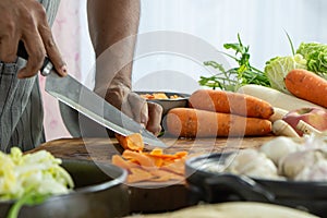 hand of man with a knife cut a fresh carrot with vegatable for cooking copy space