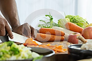 hand of man with a knife cut a fresh carrot with vegatable for cooking copy space