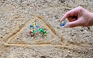 The hand of a man playing marbles in a playground with dirt