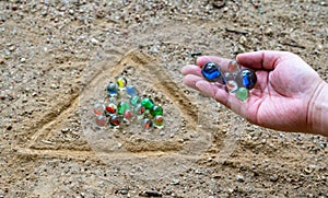 The hand of a man playing marbles in a playground with dirt