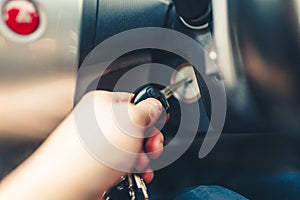 Hand man plug in a key starting the engine of a car.