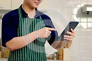 Hand man pointing at digital tablet, baker wearing apron and searching tasty meal and bake bread recipes on internet, chef cooking